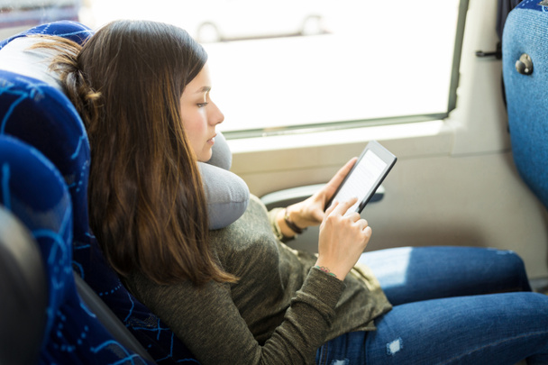 Female resting with neck pillow while reading e-book in bus - Photo, image