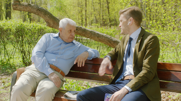 Yaşlı adam ve genç adam parktaki bankta konuşuyorlar. - Video, Çekim
