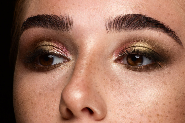 Close-up of woman's eyes with evening make-up. Fashionable shades of eye shadow, extremely long eyelashes and thick smooth eyebrows. Open beautiful look. Clean skin and freckles on face - Zdjęcie, obraz