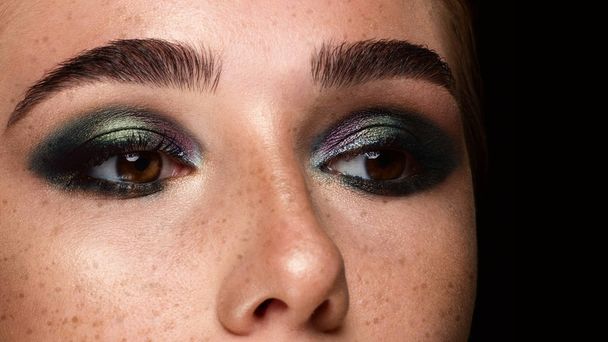 Close-up of woman's eyes with evening make-up. Fashionable shades of eye shadow, extremely long eyelashes and thick smooth eyebrows. Open beautiful look. Clean skin and freckles on face - Foto, Imagem