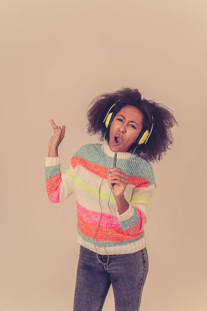Colorful portrait of gorgeous and happy african american woman listening to smart phone music app in headphones singing and dancing on neutral background. In people Music Technology and Happiness. - Foto, Imagem