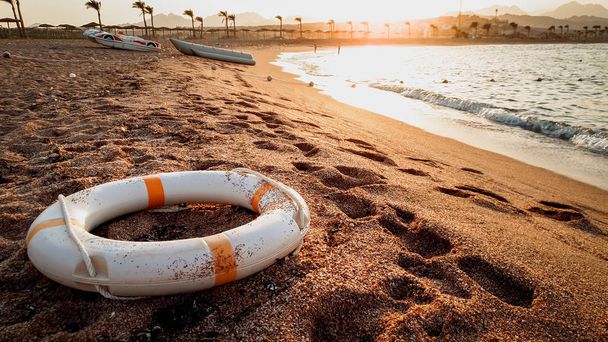 Крупним планом тоноване зображення рятувального кільця, що лежить на морському піску. Красивий захід сонця над океаном
 - Фото, зображення
