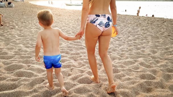 Piękny obraz szczęśliwy uśmiechnięty 3 lat chłopiec maluch chodzenie i relaks na piaszczystej plaży morskiej o zachodzie słońca. Rodzina ma dobry czas podczas letnich wakacji na plaży - Zdjęcie, obraz