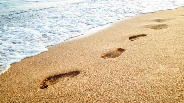 Closeup photo of calm sea waves washing off human footprints on wet sand at sandy sea beach - Photo, Image