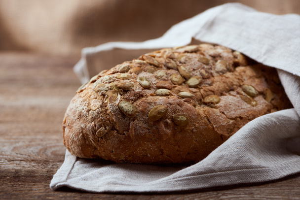 fresh baked bread with seeds in white napkin on wooden table - Foto, afbeelding