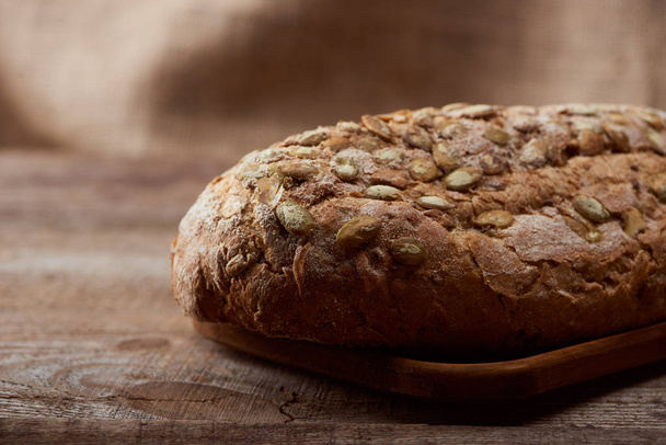 close up view of fresh baked bread with seeds on wooden table - Foto, afbeelding