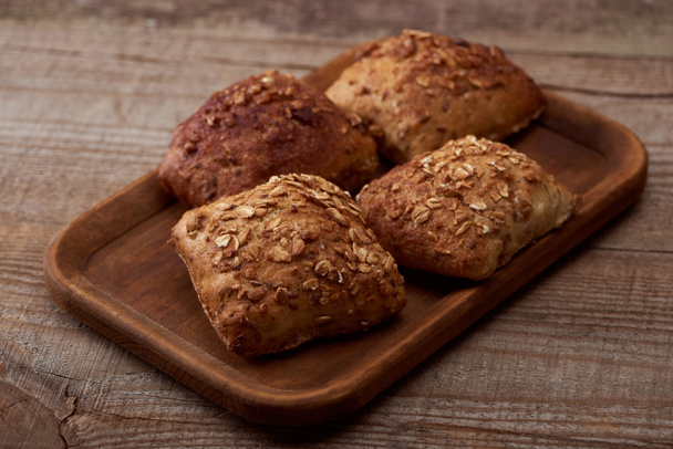 fresh baked buns with grains on wooden board on rustic table - 写真・画像
