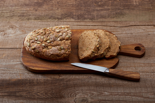 fresh cut loaf of bread with seeds on chopping board near knife on wooden table - 写真・画像