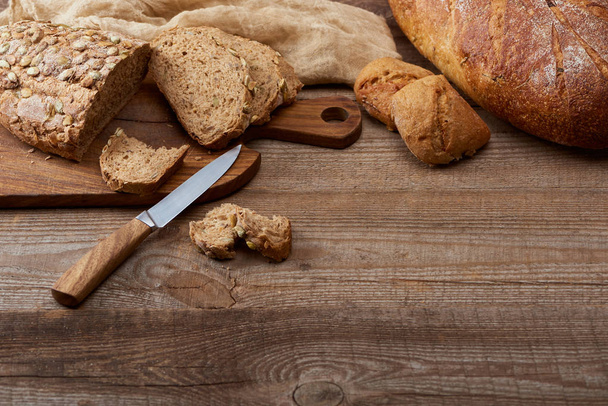 свіжий нарізаний і цільний хліб хліб хліб і булочки, ніж і подрібнювальна дошка біля тканини на дерев'яному столі
 - Фото, зображення