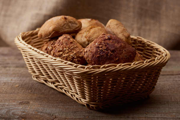 delicious bread and buns in wicker box on wooden table - Fotoğraf, Görsel