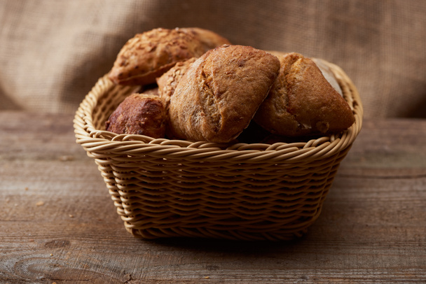 fresh baked buns in wicker basket on wooden table with sackcloth on background - Valokuva, kuva