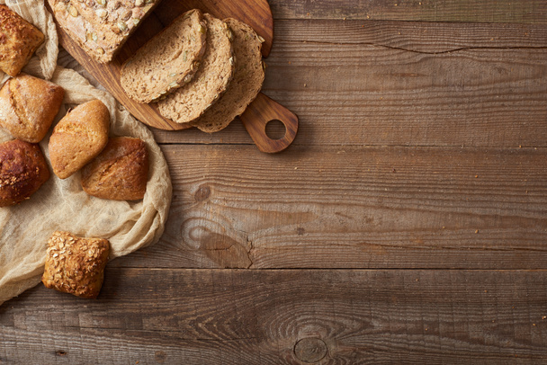 Κορυφαία θέα από φρέσκο ψωμί φέτες σε σανίδα κοπής και ψωμάκια σε πανί σε ξύλινο τραπέζι - Φωτογραφία, εικόνα