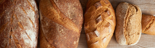 pohled na čerstvé domácí bochníky chleba a housky na dřevěném venkovním stole, panoramatický záběr - Fotografie, Obrázek