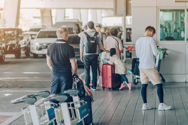 大きなローラーの荷物を持つ乗客は、空港到着ターミナルで車がピックアップするのを待つために立ちます. - 写真・画像