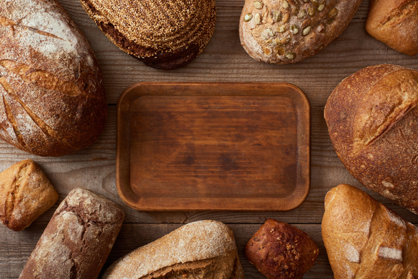 top view of fresh homemade loaves of bread around wooden empty chopping board - Φωτογραφία, εικόνα