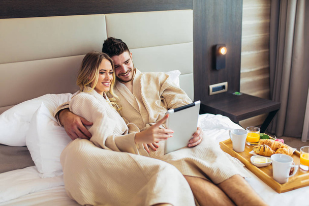 Joven pareja feliz compras en línea en habitación de hotel de lujo
.  - Foto, Imagen