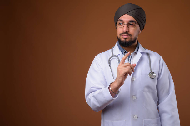 Young bearded Indian Sikh man doctor wearing turban against brow - Fotografie, Obrázek