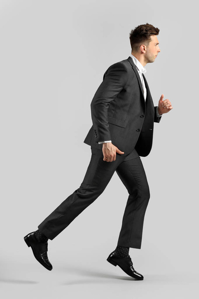 Running young businessman on grey background - Foto, Imagen
