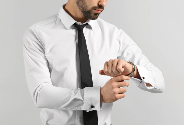 Модний молодий чоловік дивиться на свій годинник на сірому фоні
 - Фото, зображення