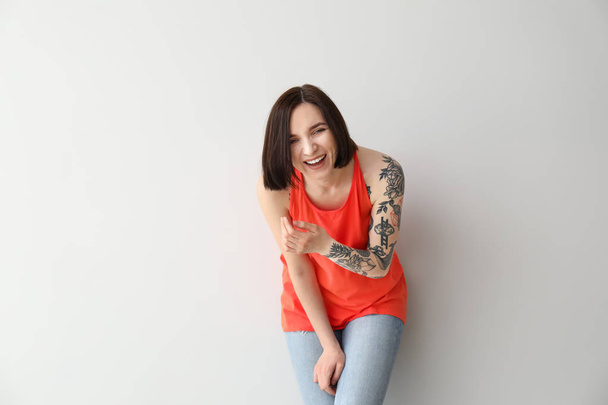 Κομψή γυναίκα με τατουάζ σε ανοιχτόχρωμο φόντο - Φωτογραφία, εικόνα