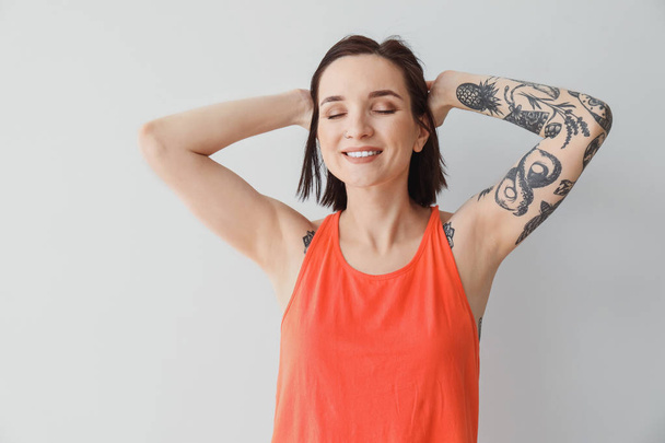 Stylish tattooed woman on light background - Photo, Image