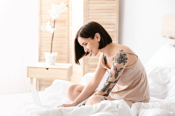 Morning of beautiful tattooed woman with laptop in bedroom - Photo, Image