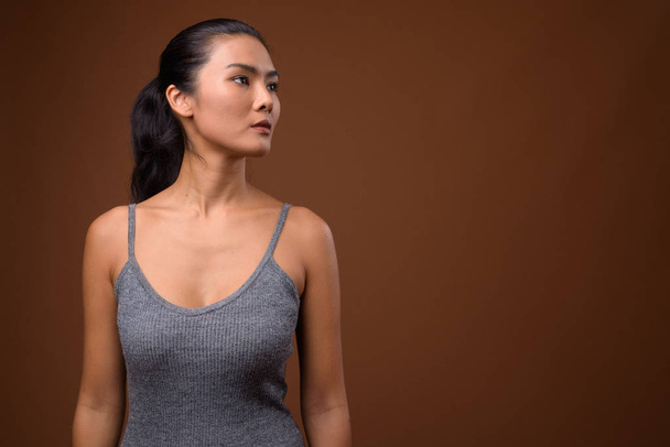 Studio strzał pięknej azjatyckiej kobiety przed brązowym tłem - Zdjęcie, obraz