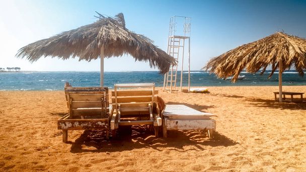 Bela foto de antigas espreguiçadeiras ou espreguiçadeiras de madeira na praia vazia no dia ensolarado ventoso
 - Foto, Imagem