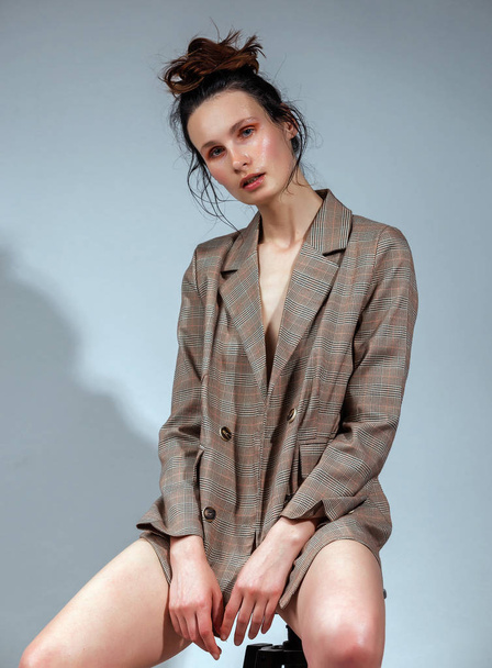 Roztomilá brunetka, která nosí kabát přes své nahé tělo a vysoké spodní prádlo Pózované ve studiovém módu a konceptu krásy - Fotografie, Obrázek
