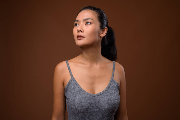 Studio shot of beautiful Asian woman against brown background - Valokuva, kuva