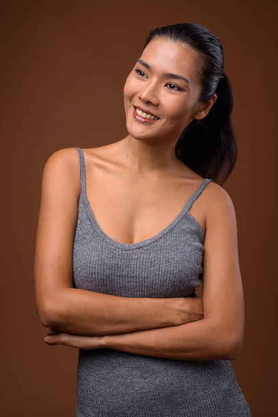 Studio shot of beautiful Asian woman against brown background - Photo, image