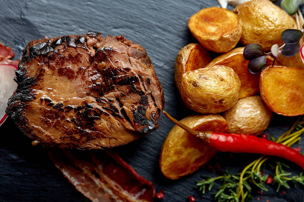 Beef steak served with baked potatoes and vegetables,black background, close-up. concept food. - Photo, Image