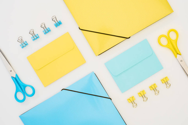 top view of yellow and blue envelopes, folders, paper clips and scissors isolated on white  - Foto, afbeelding