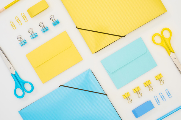 плоская укладка голубых и желтых папок, конвертов, ножниц, карандашей, ластиков и скрепок, изолированных на белом
 - Фото, изображение