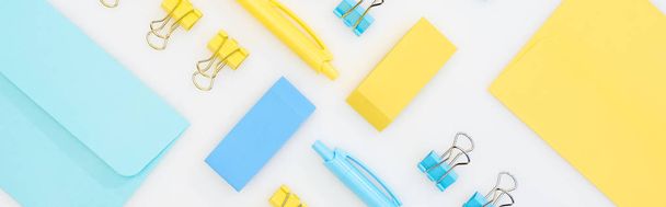panoramic shot of yellow and blue erasers, pens, envelopes and paper clips isolated on white - Photo, Image