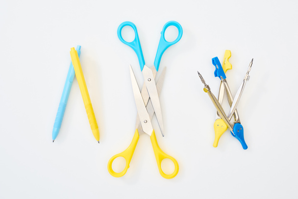 вид сверху на желтый и синий ножницы, ручки и компасы на белом фоне
 - Фото, изображение