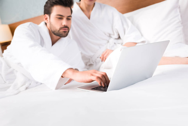 selective focus of bearded man using laptop near woman in hotel room  - 写真・画像
