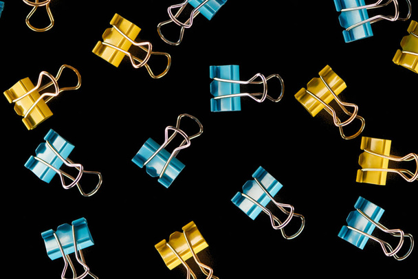 top view of colorful scattered yellow, orange and blue paper clips isolated on black  - Photo, Image
