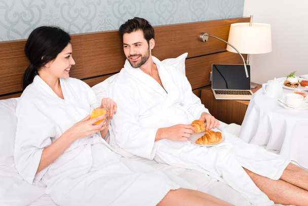 cheerful man holding croissants while looking at woman with glass of orange juice  - Photo, Image