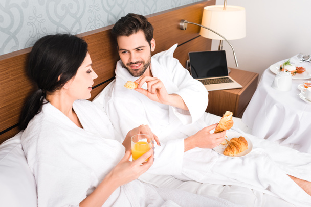 cheerful man holding croissant while looking at attractive woman with glass of orange juice  - Φωτογραφία, εικόνα