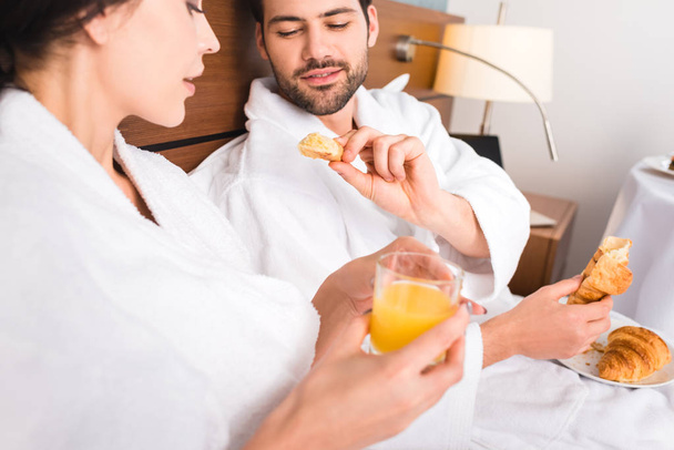 selektiver Fokus des Mannes mit Croissant in der Nähe der attraktiven Frau mit einem Glas Orangensaft - Foto, Bild