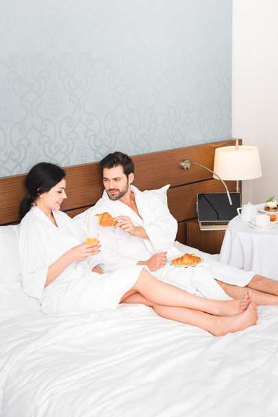 bearded man holding croissant near happy woman with glass of orange juice - Foto, Imagem