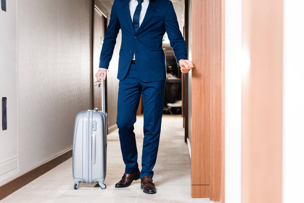 cropped view of businessman holding hotel card while standing near suitcase  - Φωτογραφία, εικόνα