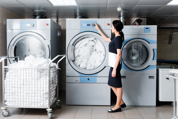 alegre mucama tocar botón en la lavadora en la lavandería
  - Foto, Imagen