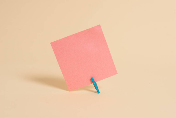 Plain note paper and clip placed above a pastel backdrop. Empty sheet plus stationary stick to soft hued background in tilted position. Artistic way of flat lays photography - Photo, Image