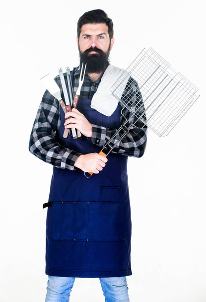 Barbecue season. Bearded hipster wear apron for barbecue. Roasting and grilling food. Man hold cooking utensils barbecue. Tools for roasting meat outdoors. Picnic and barbecue. Tips for cooking meat - Foto, Bild