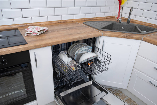 Открытая посудомоечная машина с грязной посудой на белой кухне
 - Фото, изображение