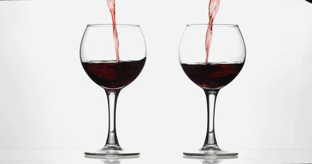 Rose wine. Red wine pour in two wine glasses over white background - Photo, Image