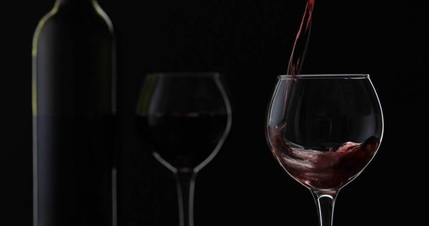 Розовое вино. Красное вино наливают в бокал вина на черном фоне. Силуэт
 - Фото, изображение