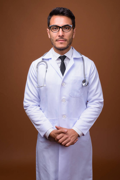 Joven guapo hispano hombre doctor contra marrón fondo - Foto, Imagen
